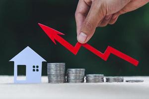 Hand, die ein Diagramm über der zunehmenden Hausminiatur hält. immobilieninvestitionen und haushypothekenfinanzkonzept, als finanzinvestition gehaltene immobilien, immobilien. foto