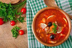 suppe solyanka russisch mit fleisch, oliven und gurken in holzschale foto