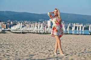 Blonde Frau im Kleid steht am Sandstrand am Meer und genießt den Blick auf den Sonnenuntergang. foto