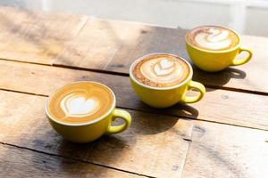 Latte-Kaffee oder Cappuccino-Kaffee in gelber Tasse mit schöner Herz-Latte-Kunst auf Holztisch. foto