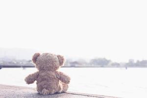 ein trauriger teddybär sitzt allein auf einer brücke und blickt einsam mit kopierraum auf das meer. Spielzeug, Puppe, für Kinder. foto
