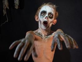 Studioaufnahme Porträt eines kleinen Jungen in Kostümen, die als Halloween verkleidet sind, Cosplay einer gruseligen Mumienpose auf isoliertem schwarzem Hintergrund foto