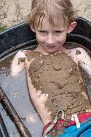 kleiner Junge spielt im Schlamm in einer mit Wasser gefüllten Schubkarre foto