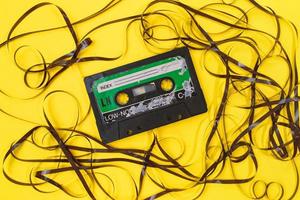 Altes Retro-Kassettenband mit Grunge-Etikett, umgeben von gezogenem Bandstapel auf gelbem Hintergrund, flach gelegt foto
