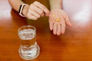 Frauenhände, die Vitamin-C-Pillen mit einem Glas Wasser auf dem Tisch halten. foto