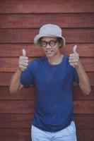 asiatischer Mann unterschreibt guten Daumen mit lustigem Gesicht vor altem Holzhintergrund foto