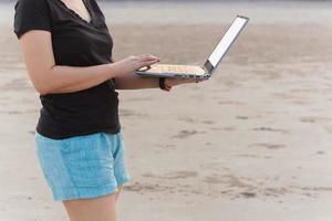 freiberuflerin, die am strand steht und mit laptop arbeitet. foto