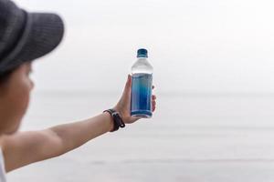 Frau mit Flasche Mineralwasser in der Hand am Strand. foto