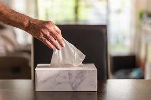 Hand des älteren Mannes, der Seidenpapier aus der Taschentuchbox auf dem Esstisch aufhebt. foto