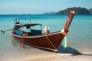 nicht identifizierte Frau sitzt auf einem Holzboot im Meer Sonnenbaden. foto