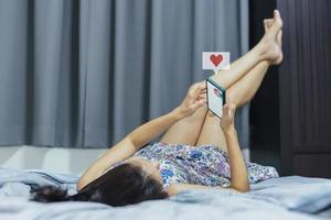 Frau liegt im Bett mit Smartphone mit Herz-Symbol Valentinstag-Konzept. foto