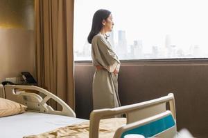 depressive asiatische Patientin steht auf der Krankenstation und schaut aus dem Fenster. foto