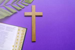 Kreuz und Bibel mit Palmblättern auf violettem Hintergrund. Konzept der Karwoche. foto