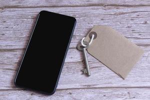 Braunes Etikett mit Schlüssel und Smartphone auf einem Schreibtisch. flach liegen. für Texte foto