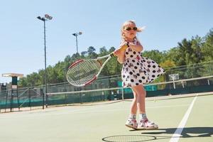 süßes kleines Mädchen, das draußen auf dem Tennisplatz Tennis spielt foto