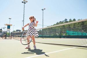 süßes mädchen, das tennis spielt und für die kamera posiert foto