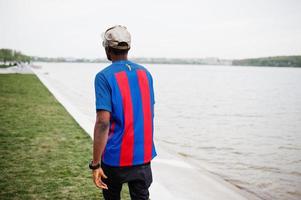 stylischer afroamerikanischer Junge trägt Kappe, Fußball-T-Shirt und Sonnenbrille. schwarzes Sportlerporträt. foto