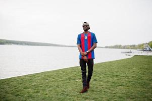 stylischer afroamerikanischer Junge trägt Kappe, Fußball-T-Shirt und Sonnenbrille. schwarzes Sportlerporträt. foto