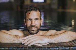Porträt eines lächelnden jungen Mannes, der sich am Rand des Swimmingpools entspannt foto