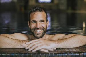 Porträt eines lächelnden jungen Mannes, der sich am Rand des Swimmingpools entspannt foto