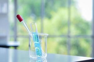 Reagenzglas mit blauer Chemikalie im Inneren wurde mit einer Pipette und einem Glasstab im Inneren des Bechers auf dem Tisch im Chemielabor platziert, um das Experiment vorzubereiten foto