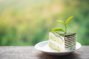 Close-up-Teeblatt auf Matcha-Grüntee-Zweischicht-Biskuitkuchen und Sahne mit Matcha-Grüntee-Pulver, das in einer weißen Platte auf einem Holztisch bestreut wird. foto