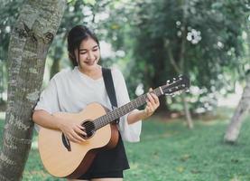asiatische junge frau, die gitarre spielt und musik im park singt, asiatische frau, die gitarre im garten spielt