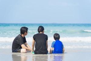 familie asiatisch am strand sitzend mit blick auf das blaue meer, die insel, das sonnenlicht und den blauen himmel am morgen. foto