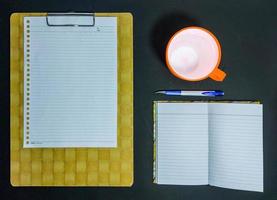 Papier, Buch, Stift und eine Tasse Mineralwasser auf schwarzem Hintergrund foto