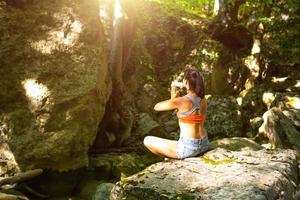 Eine Frau sitzt in einem Lotusfeld auf einem großen Felsen zwischen den Felsen im Freien und meditiert, genießt die Einheit mit der Natur, lauscht der Stille und den Geräuschen des Waldes. Ökologie foto