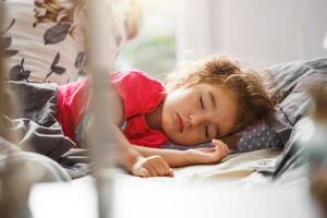 ein kleines Kind schläft süß in seinem Bett. gesunder Schlaf des Mädchens, Belüftung. Morgen, aufwachen, Sonnenlicht aus dem Fenster. früher Aufstieg in Kindergarten, Schule. foto