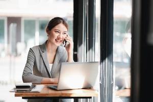 porträt einer jungen asiatischen geschäftsfrau, die sich auf dem smartphone mit einem notebook-laptop im home office unterhält. schönes mädchen am schreibtischcomputer mit nach hause bestellen. startup business asien frau online sme telemarketing. foto