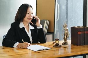 junge schöne asiatische rechtsanwältin, die im büro arbeitet. mit dem Kunden auf einem Smartphone sprechen. foto