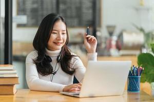 seitliche vire einer glücklichen hübschen frau mit dunklem lockigem haar, die einen videoanruf von zu hause aus hat, mit headset und laptop im wohnzimmer spricht, mit freunden oder verwandten spricht, kopierraum foto