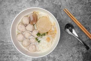 Draufsicht Reisfadennudelsuppe mit Schweinefleischbällchen in der weißen Schüssel auf dem grauen Betontisch. foto