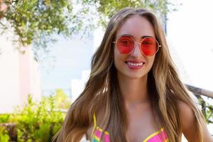 close up glückliche frau gesicht sommerferien. Sommerlächeln Mädchen mit blonden Haaren im Sommerurlaub im Badeanzug. selektiver Fokus. rosa Sonnenbrille foto