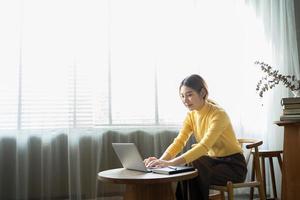 porträt einer schönen asiatischen frau, die im sommer drinnen im café-restaurant sitzt, mit intelligenter drahtloser technologie, computer-laptop und smartphone, entspannende kaffeepause im café-restaurant. foto