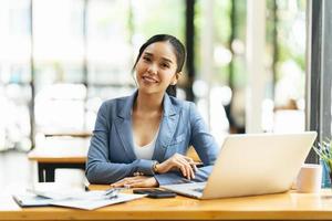 porträt einer asiatischen jungen frau, die im büro-, finanz- und investitionskonzept am laptop arbeitet. foto