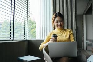 porträt einer schönen asiatischen frau, die im sommer drinnen im café-restaurant sitzt, mit intelligenter drahtloser technologie, computer-laptop und smartphone, entspannende kaffeepause im café-restaurant. foto