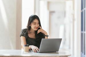 Porträt einer asiatischen jungen Frau, die im Café an Laptop und Finanzbericht arbeitet. foto