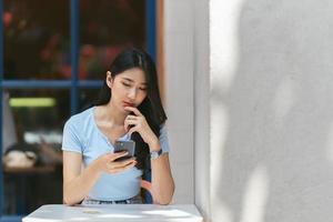 junge asiatische frau, die telefon in einem café verwendet, glücklich und lächeln. foto