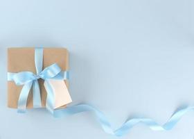 schöne Geschenkbox aus braunem Papier mit geschweifter Schleife aus blauem Satin auf pastellblauem Hintergrund. muttertag, vatertag, valentinstag, geburtstagskonzepte mit kopierraum.