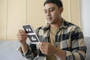 junger vater, der ultraschallfoto des neugeborenen, mutterschafts- und familienkonzeptes hält foto