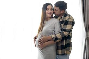 junge schwangere frau mit ehemann, die zu hause ein baby umarmt und erwartet foto