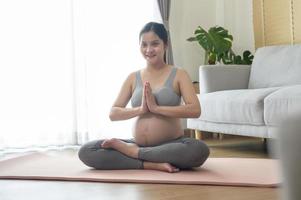 junge schwangere frau, die zu hause yoga macht, gesundheits- und schwangerschaftspflegekonzept foto