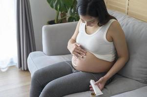 junge schwangere frau, die feuchtigkeitscreme auf bauch, gesundheitswesen und schwangerschaftspflege aufträgt foto