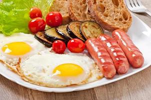 Englisches Frühstück - Spiegeleier, Würstchen, Auberginen und Tomaten foto