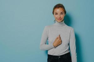 Zufriedene, zufriedene Frau zeigt auf sich, dass sie ausgewählt wurde, und erhält großartige Neuigkeiten foto