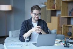 junger gutaussehender deutscher mann mit brille, der fern von zu hause aus am laptop arbeitet foto