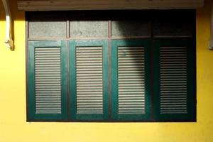 Reihe von dunkelgrünen Retro-Fenstern in rechteckiger Form und hellgelber Hauswand in Thailand. Schatten und Staub auf der Oberfläche des Fensters. foto